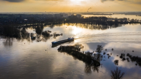 Winters landschap van rivier met hoog water met vrachtschip in werkgebied Waterschap Rijn en Ijssel